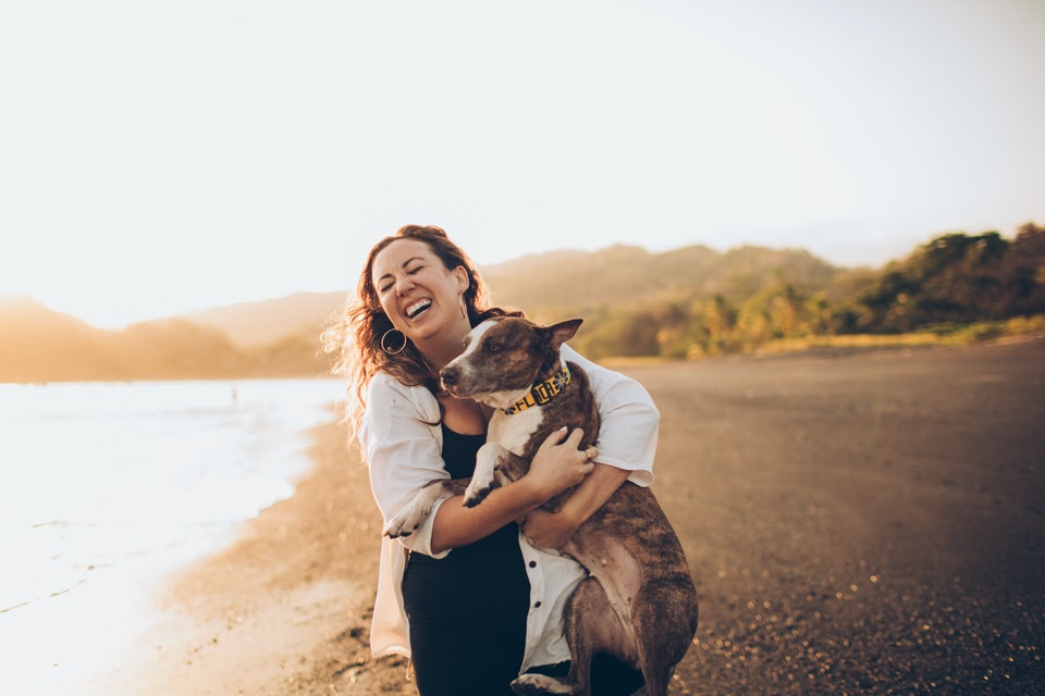 Woman laughing and holding her pet dog on the beach