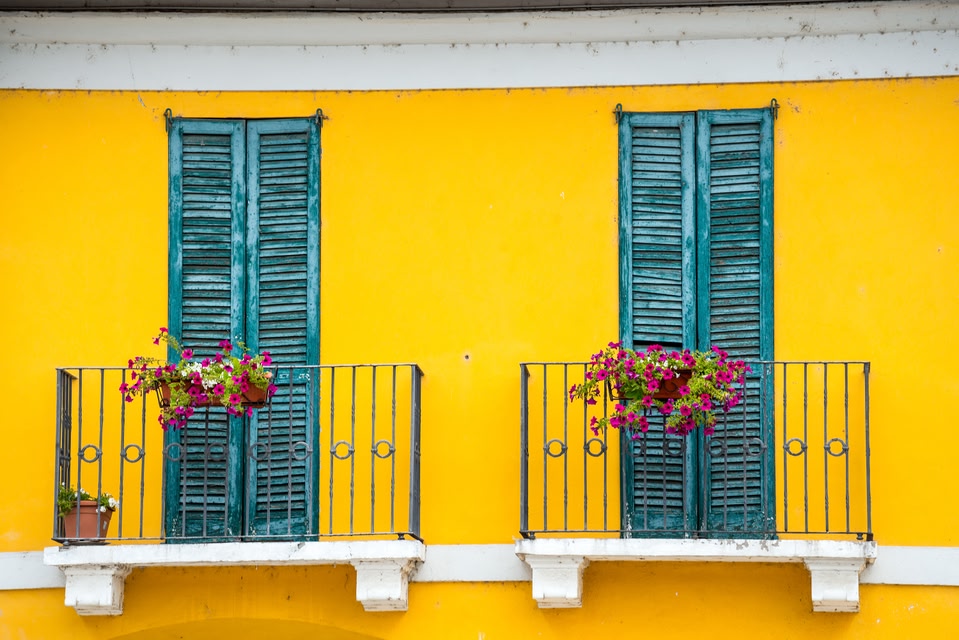 house front with yellow walls and turquoise window sills and balcony in Milan