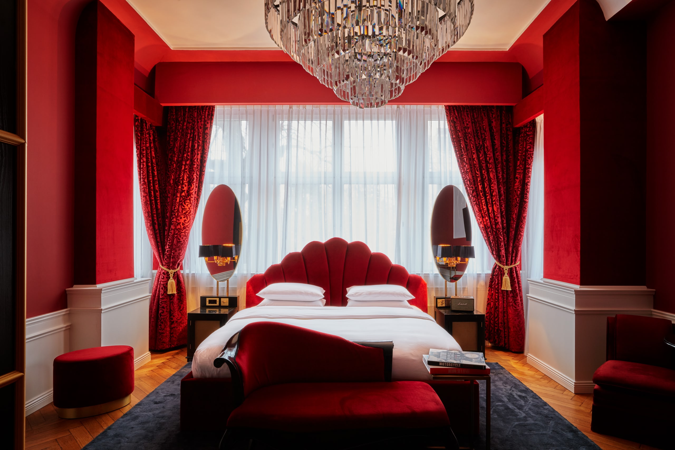 La habitación de terciopelo rojo del Hotel Provocateur. La gran cama en el centro posee una cabecera de terciopelo rojo y la ventana, que va del suelo al techo, está rodeada por cortinas y cenefas de terciopelo rojo. Una gran lámpara de araña de cristal cuelga encima de la cama.