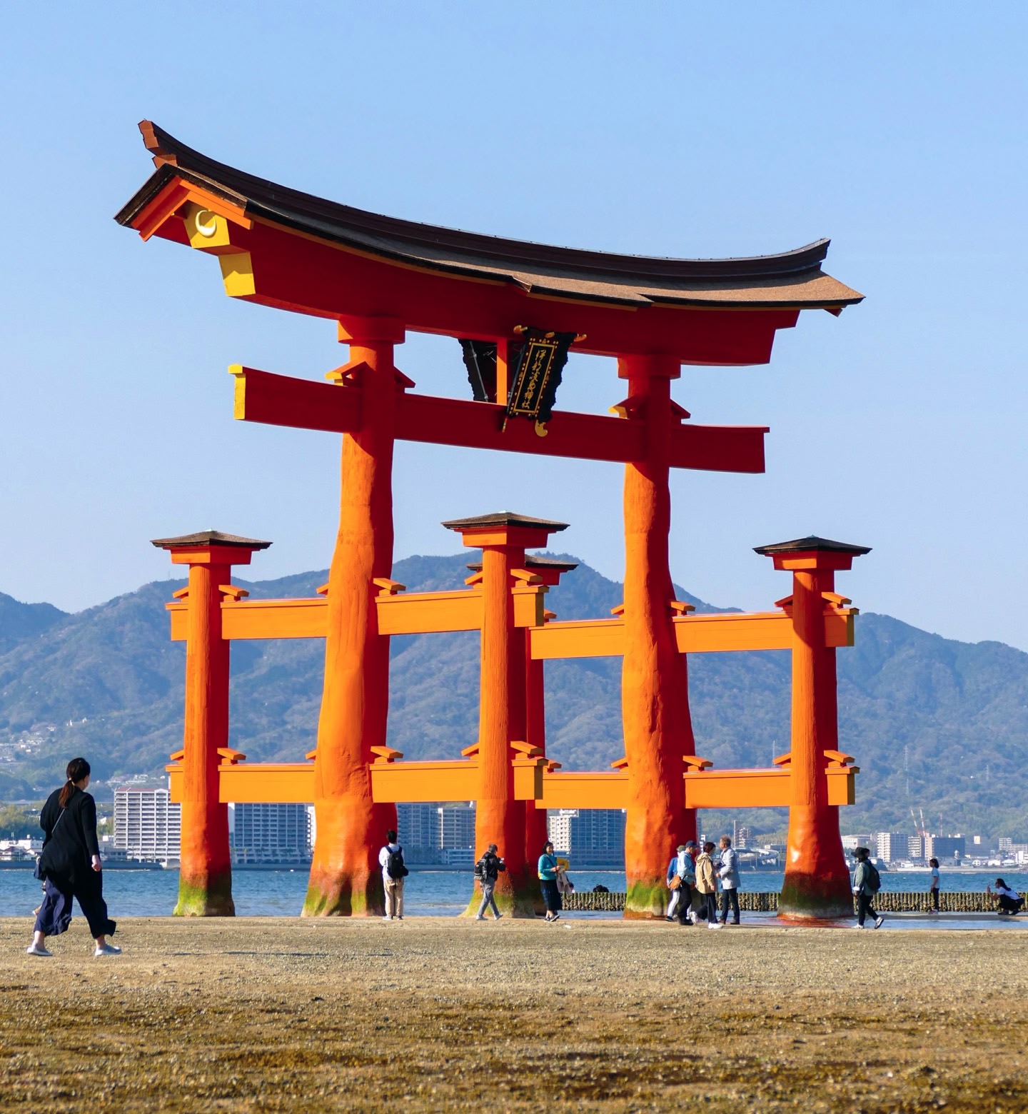 A close up view of the vibrant orange Itsukushima Shrine with people walking around it in Hiroshima, Japan