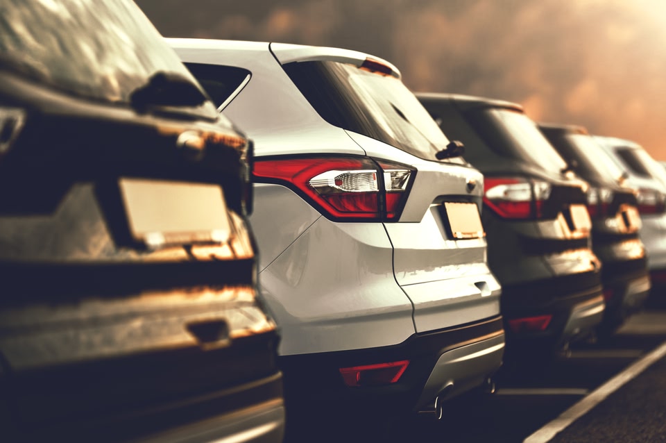 Row of parked cars in a parking lot at sunset, with warm light reflecting off their rear windows and bumpers.