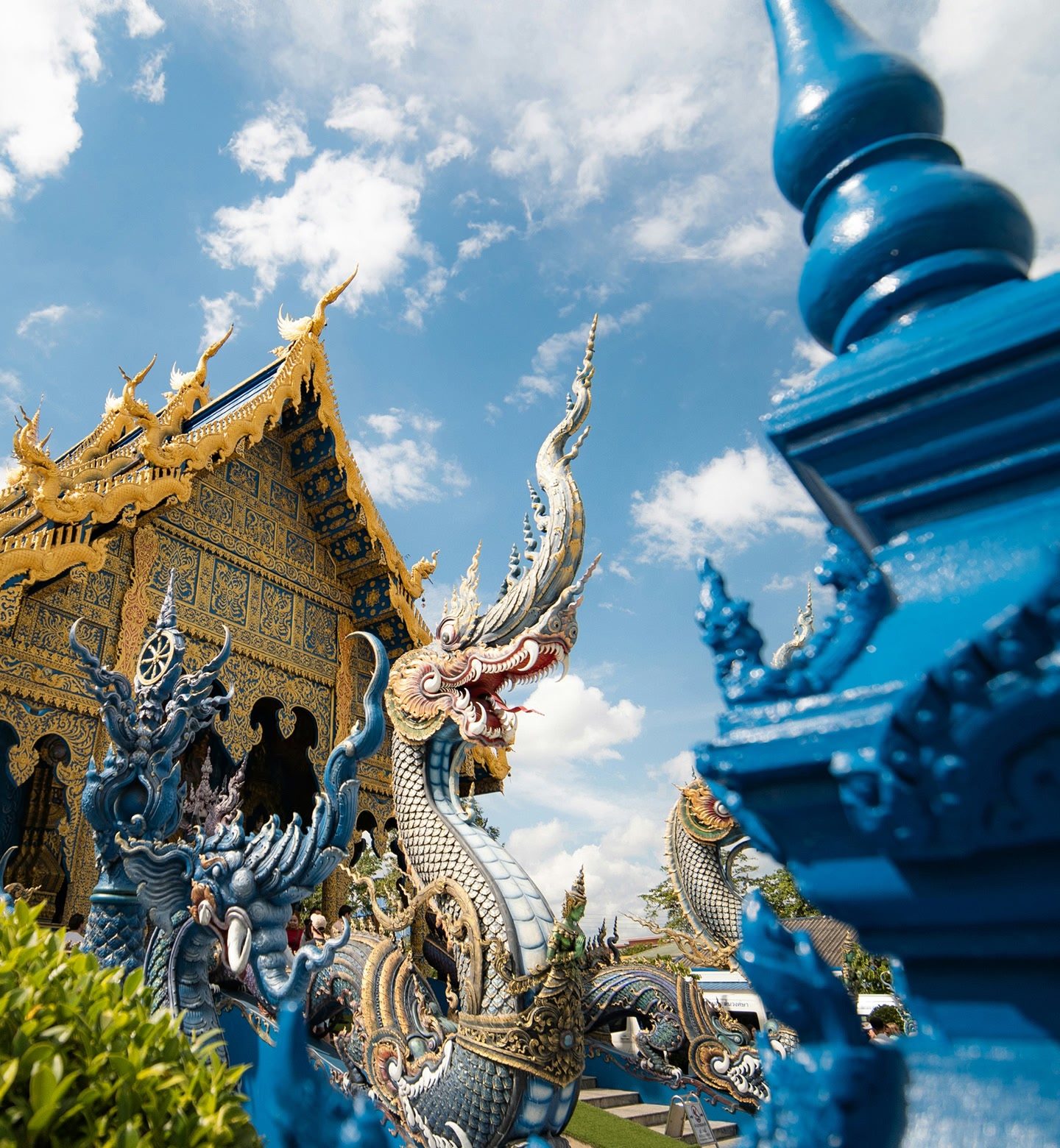 A blue pillar in front of golden dragons and an ornate temple in Chian Rai, Thailand.