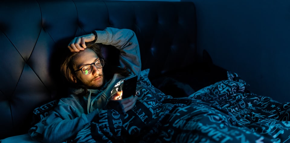 Man in bed on his phone in the dark