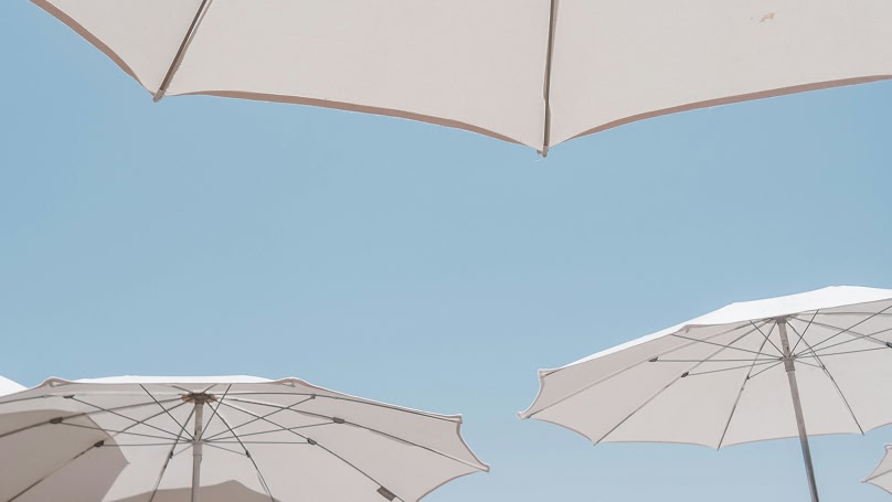 Vista dal basso di ombrelloni bianchi aperti contro un cielo azzurro chiaro
