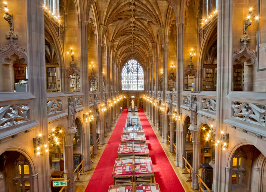 The grand walkway at the John Rylands Library with stain glass windows and high archways. 