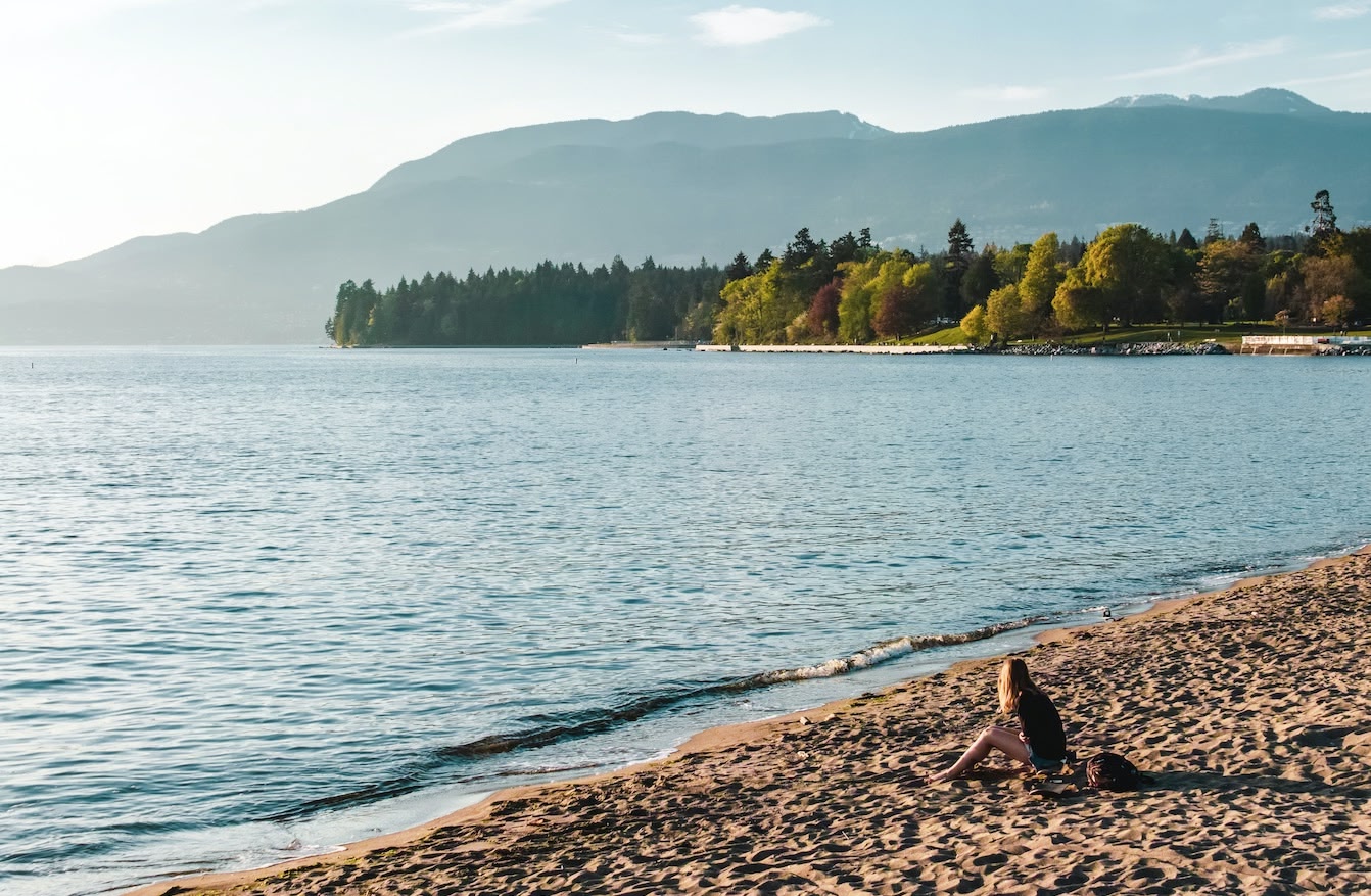 woman sitting in the sand at English Bay Beach in Vancouver, Canada. 
