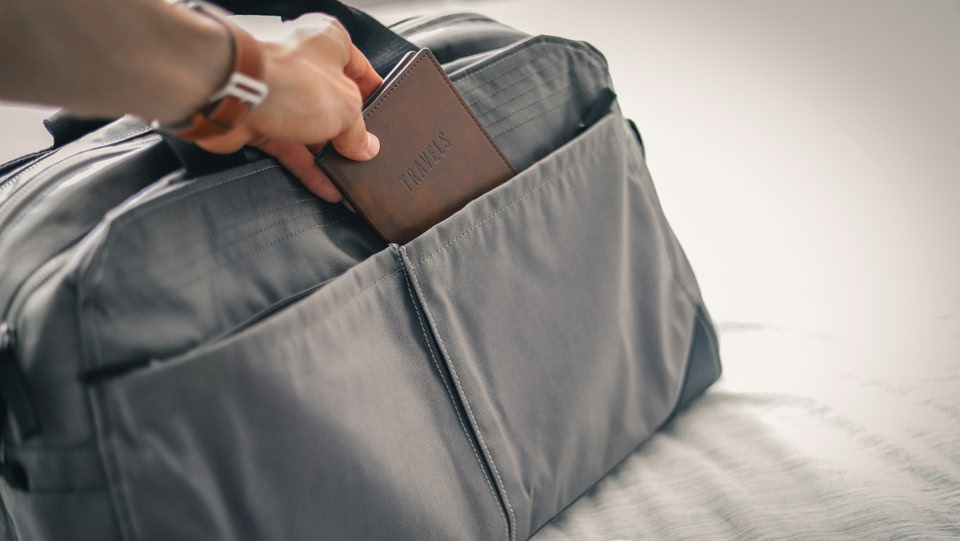 Gros plan d'une main plaçant un document de voyage dans un bagage à main.