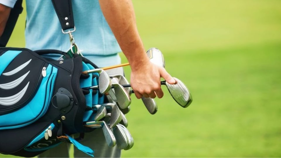 Primer plano de un golfista sosteniendo un palo junto a una bolsa de golf.