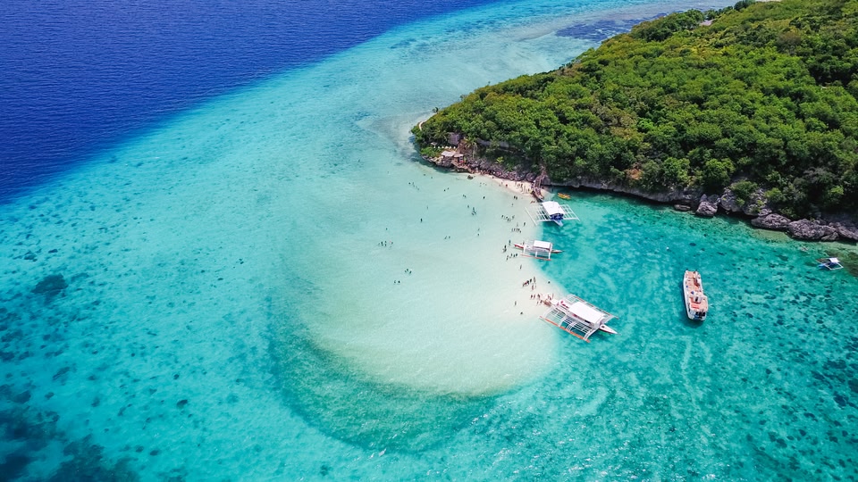 Aerial view of sandy beach with tourists swimming in beautiful clear sea water of the Sumilon island beach landing near Oslob, Cebu, Philippines. - Boost up color Processing.