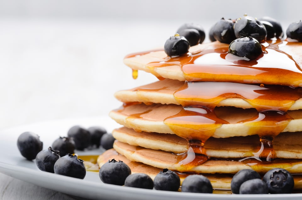 stack of pancakes with maple syrup and blueberries.