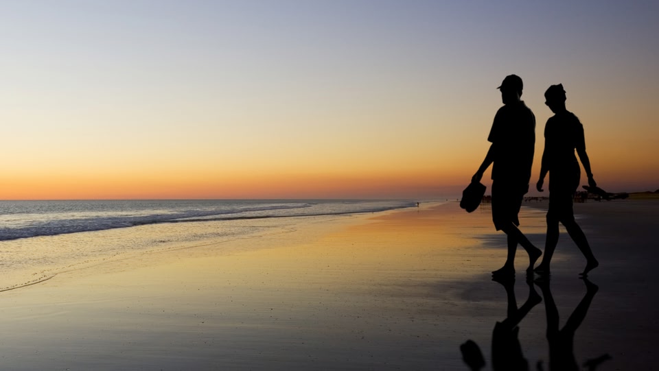 an image of two people walking on a beach at sunset 
