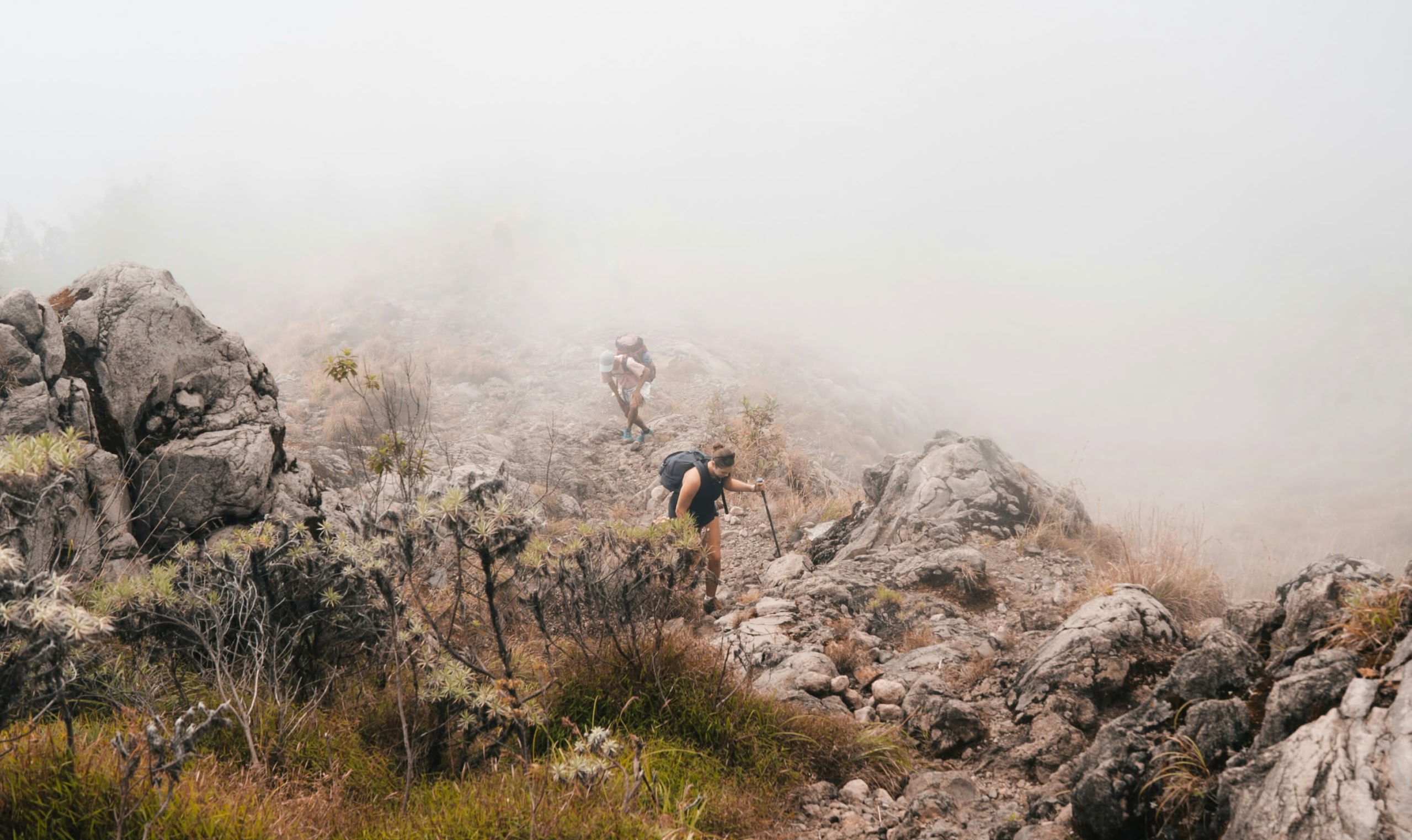 Two people hiking along a rocky path in the mist