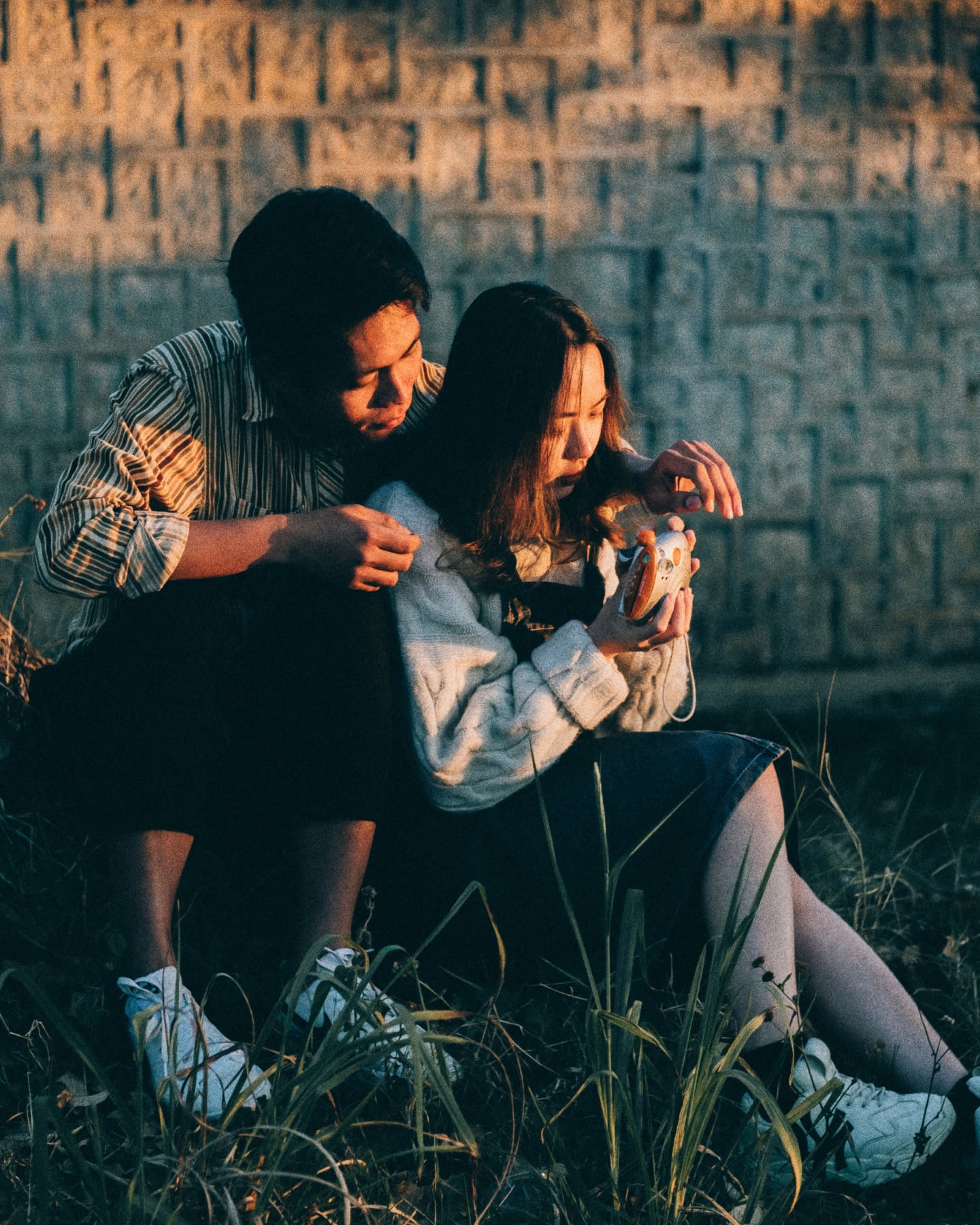 夕暮れどきに芝生に座り、一緒にカメラを見ているカップル。