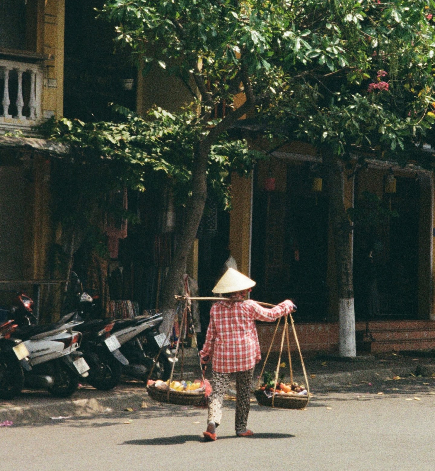 A vendor in a conical hat carries baskets of fruit along the street in Phu Quoc, Vietnam.