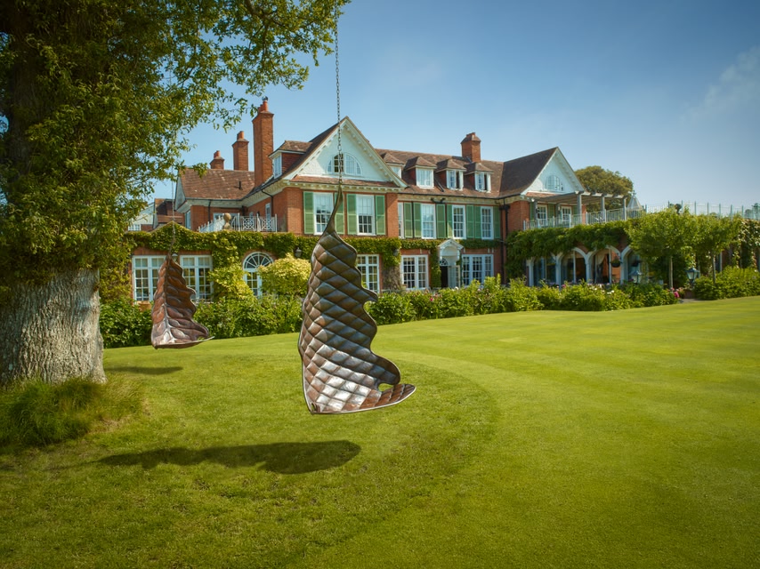 Mansion house of Chewton Glen Hotel in the background, swinging chairs in foreground, lush green lawn.