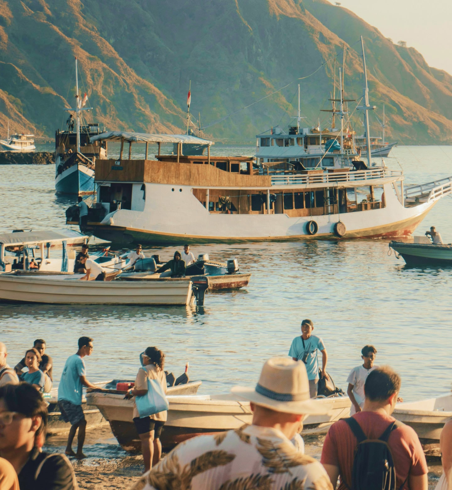 人と船が集まるインドネシアのラブハンバジョの港は、活気があふれ背後には緑の丘がある。