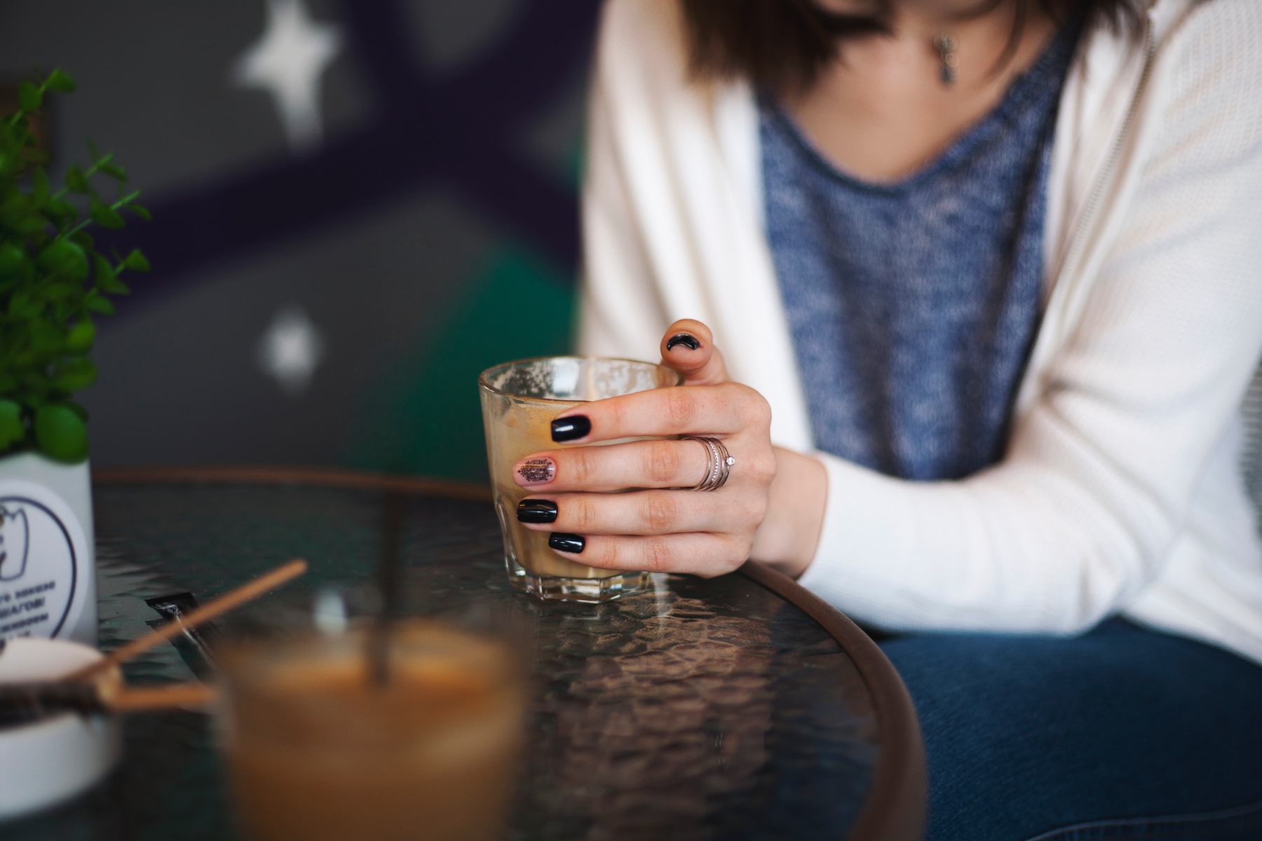 close up of person holding a cup of coffee at a coffee shop, nail polish and a ring on their finger.