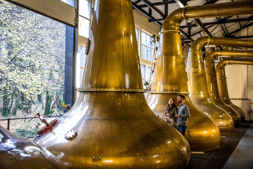 Glen Ord, the nearest distillery to Inverness & Loch Ness in the Highlands of Scotland. A couple standing next to the copper stills.