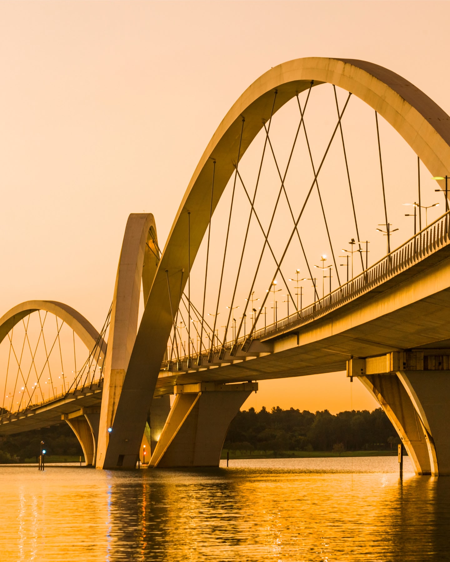 Uma ponte arqueada se estende sobre águas calmas sob um céu dourado suave em Brasília.