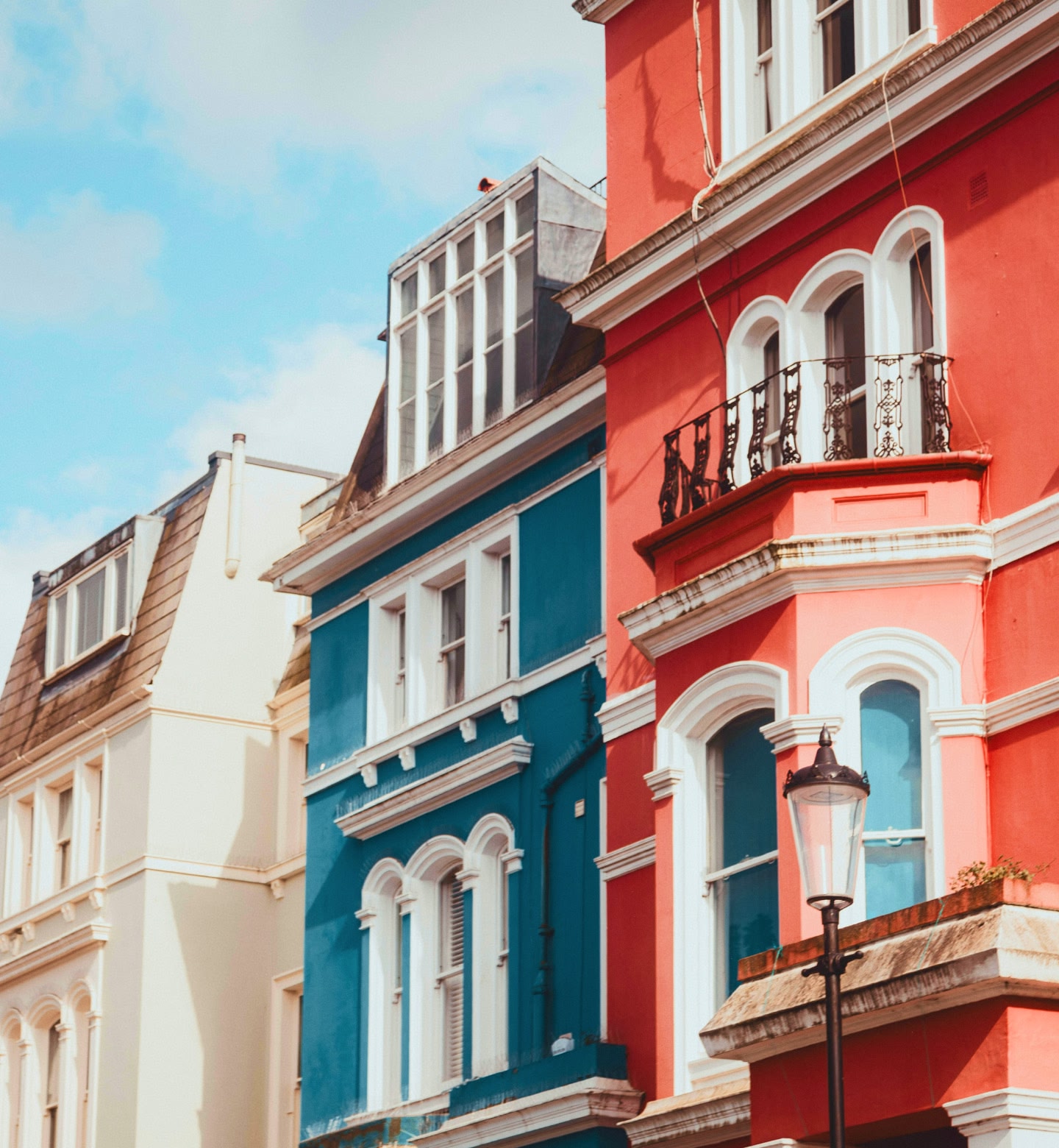 Bright townhouses in red, blue and cream line a London street.