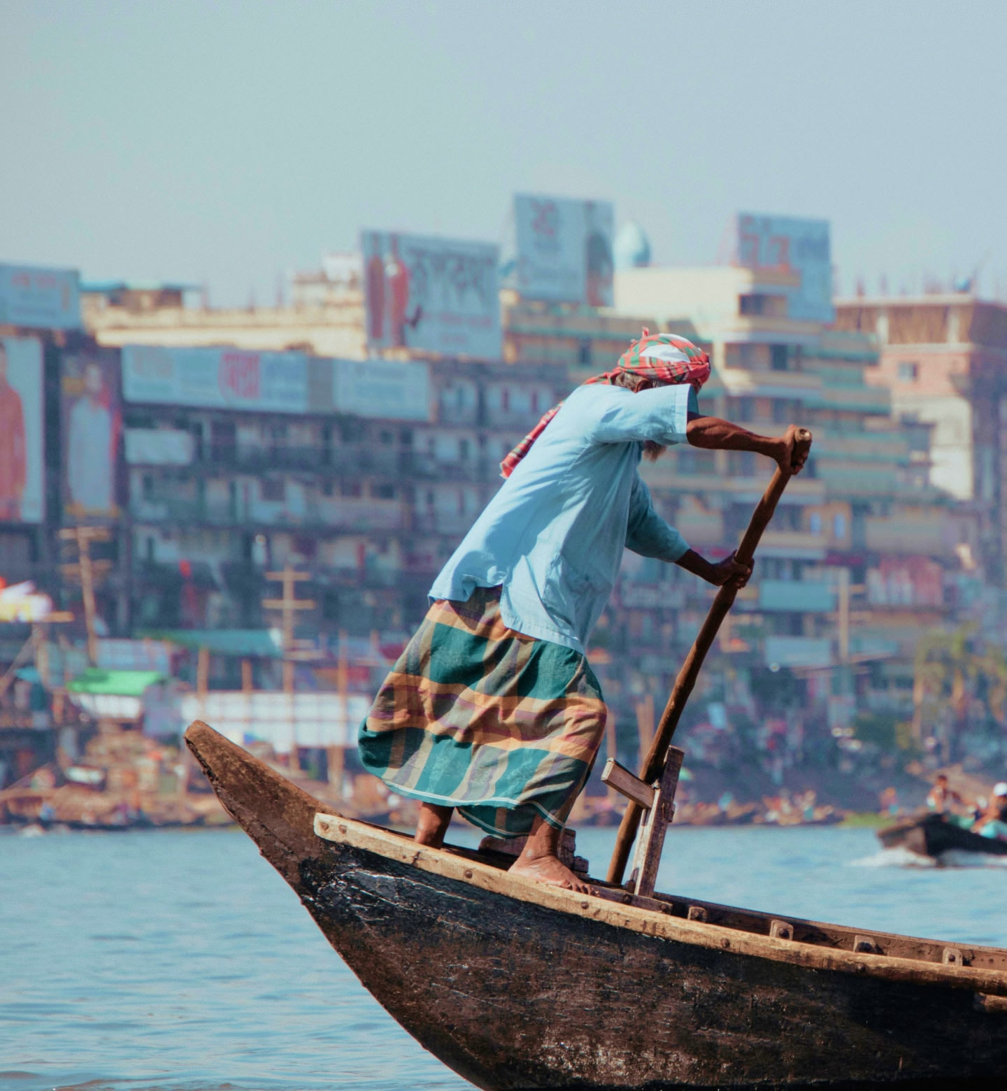 Man paddling a wooden boat along Dhaka’s waterfront, Bangladesh.
