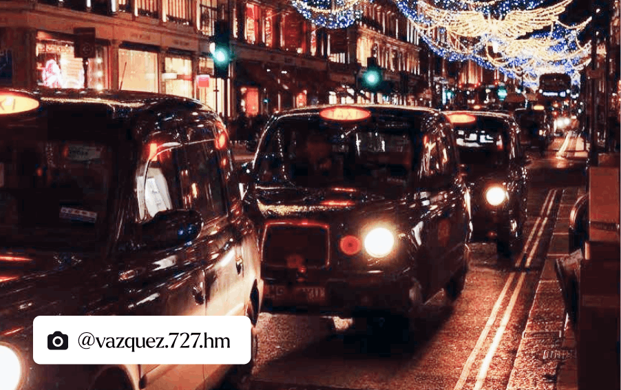 A captivating night scene in London, featuring a row of black cabs with illuminated headlights. In the background, a charming array of shops glow with warm light through their windows, accompanied by festive Christmas lights adorning the buildings.