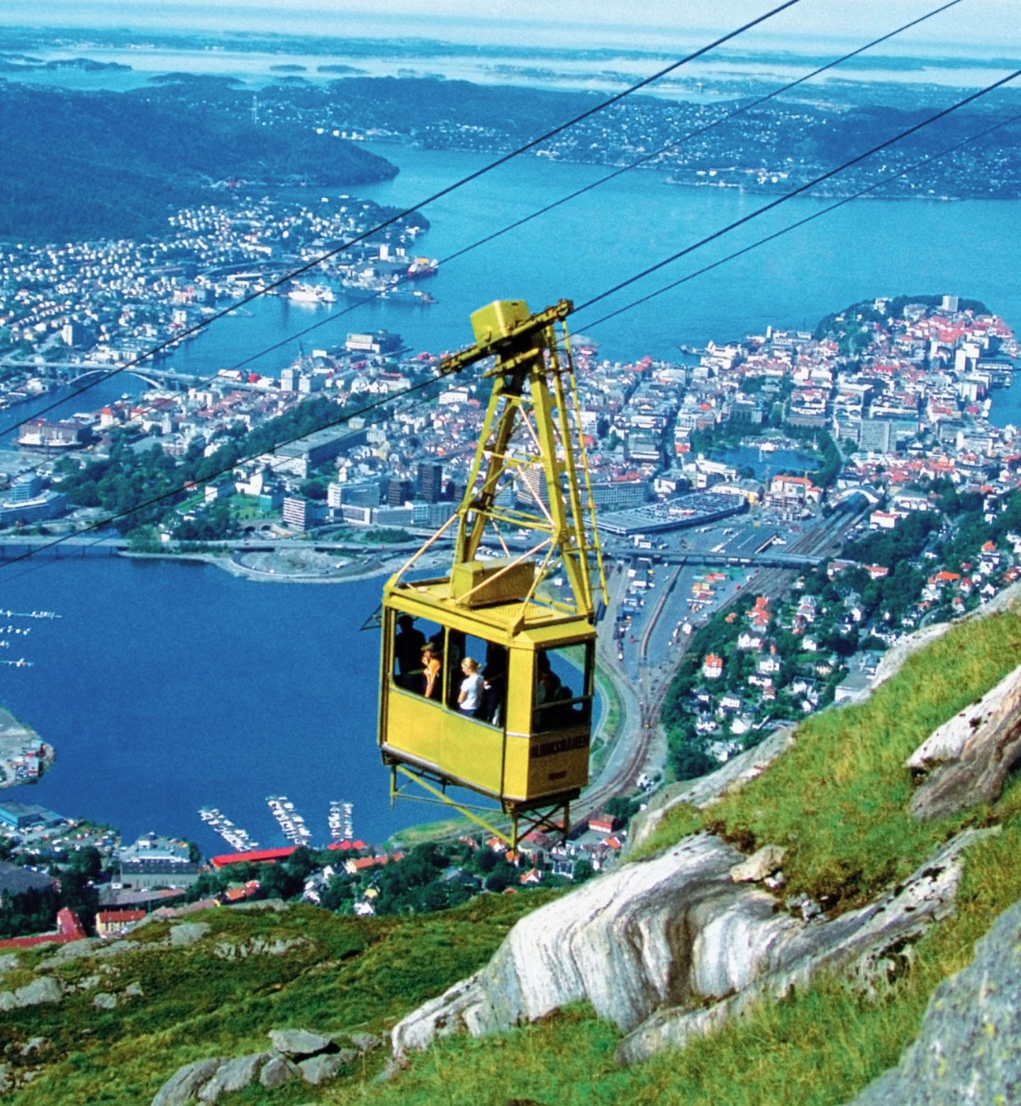 Eine gelbe Seilbahn gleitet über Bergen, Norwegen, mit Blick auf den Hafen darunter.