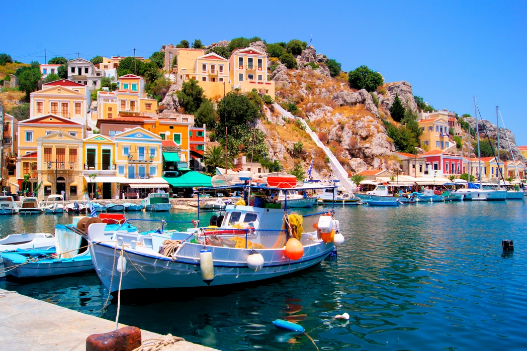 Το πολύχρωμο λιμάνι της Σύμης, ψαρόβαρκες και κτίσματα σε κίτρινους, κόκκινους και γαλανούς χρωματισμούς