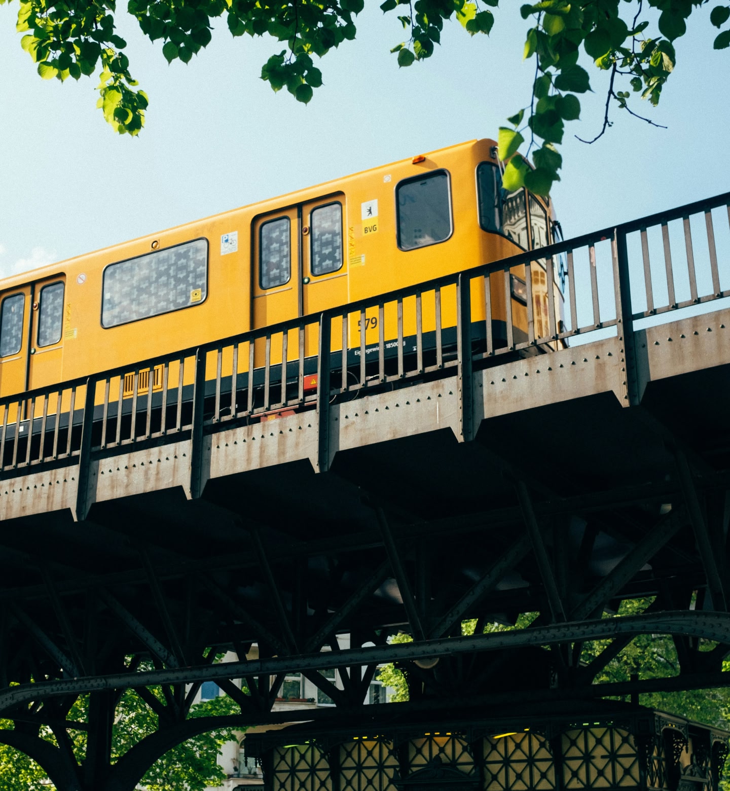 A bright yellow metro train crosses an elevated steel bridge in Berlin, Germany.