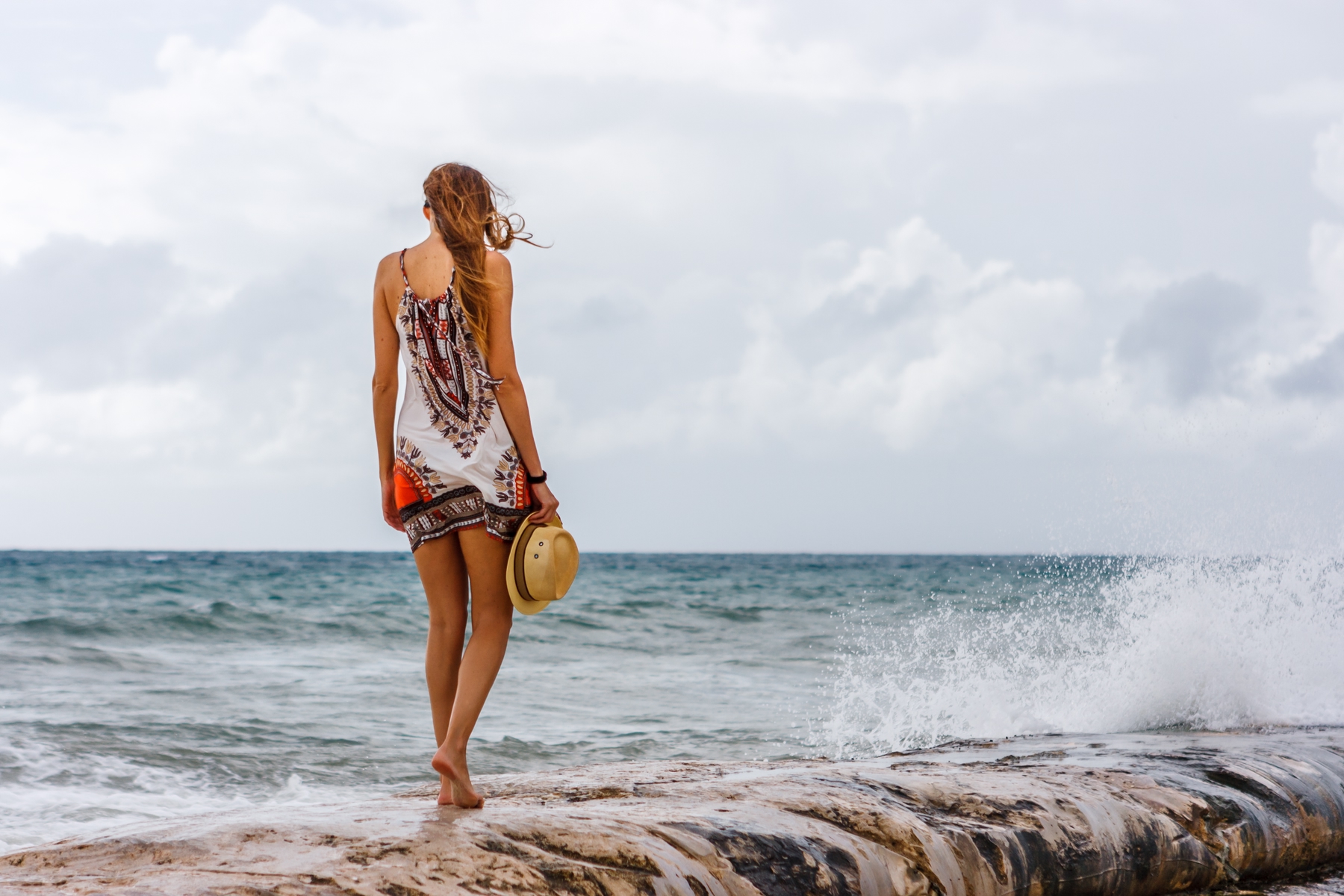 Woman with a hat in her hands staring at the sea at Playa del Carmen beach. Mexico is one of the best places to visit in May.