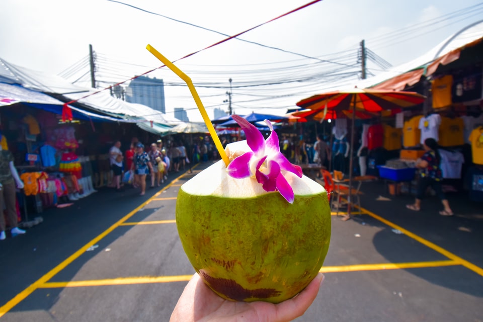 Fresh young coconut juice with orchid and a straw held by hand in Chatuchak market, Bangkok, Thailand.