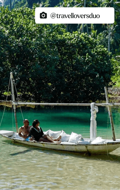 Scenic view of two people in a longboat gliding through crystal-clear waters, surrounded by lush trees