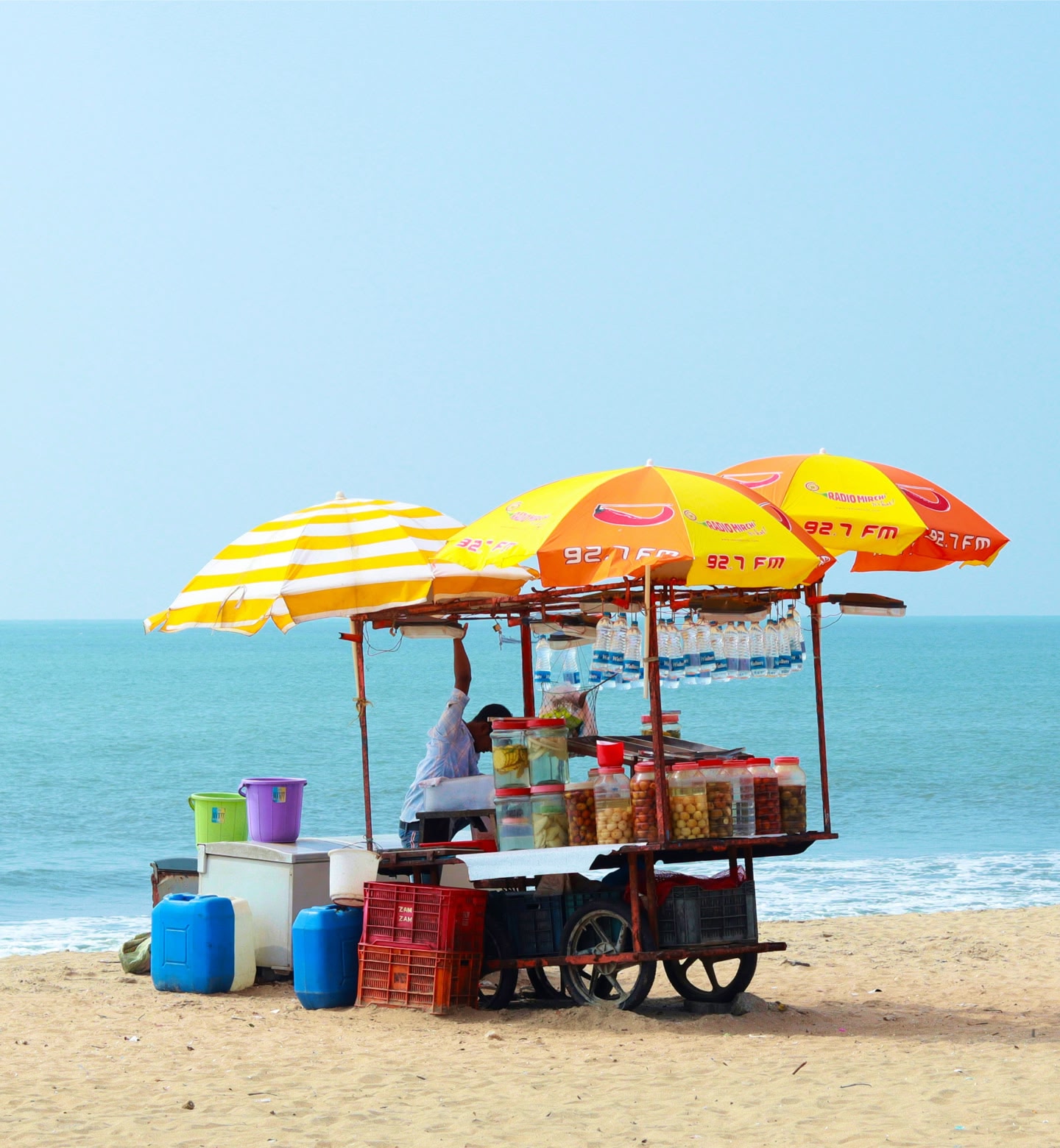 Beachside vendor cart with yellow umbrellas on a sunny day in Kozhikode, India.