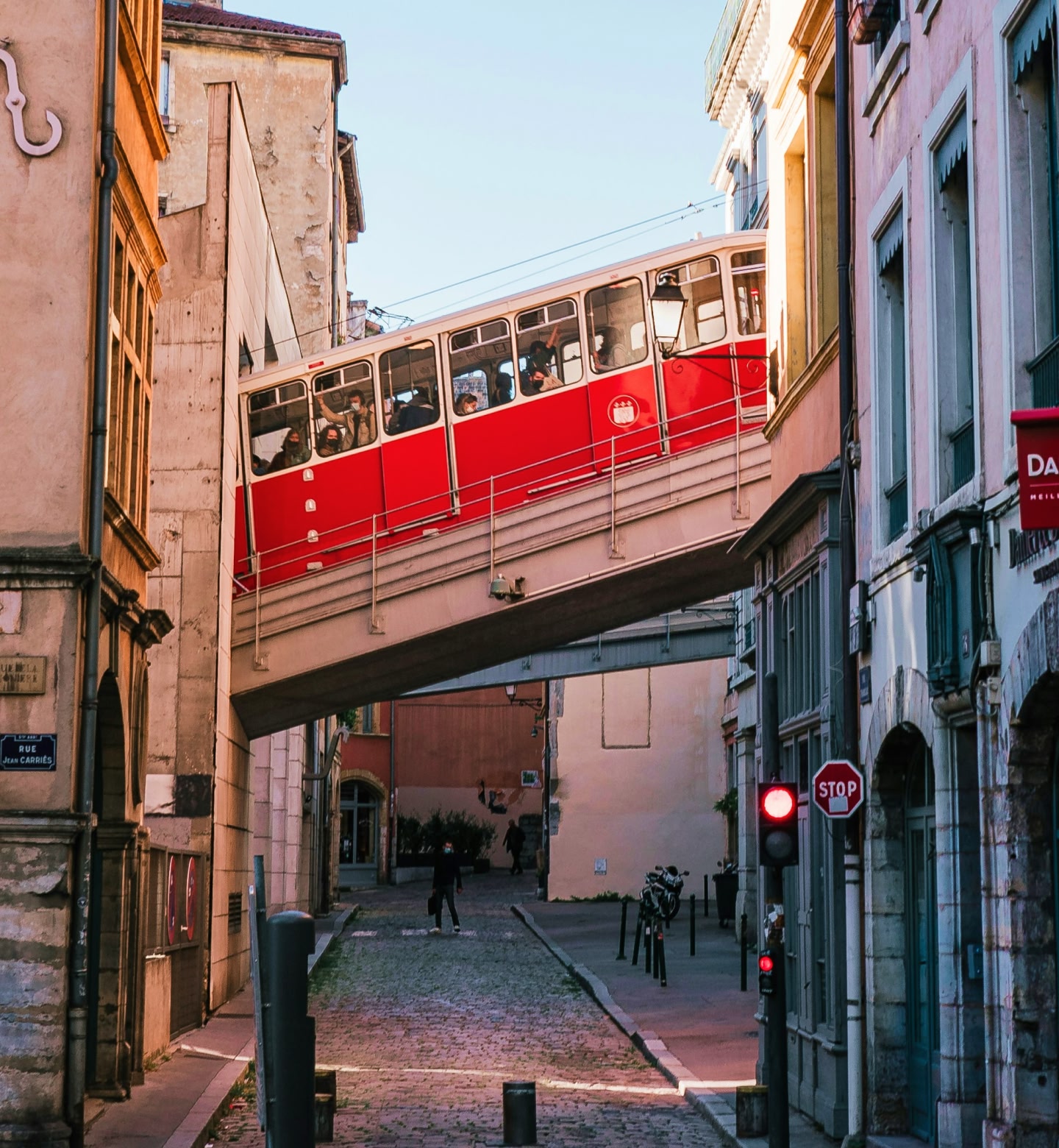 A red tram passes through a cobbled road in Lyon, France.