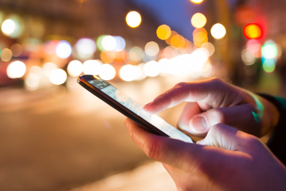 Celular na mão de um homem durante a noite - aplicativo para calcular gastos de viagem