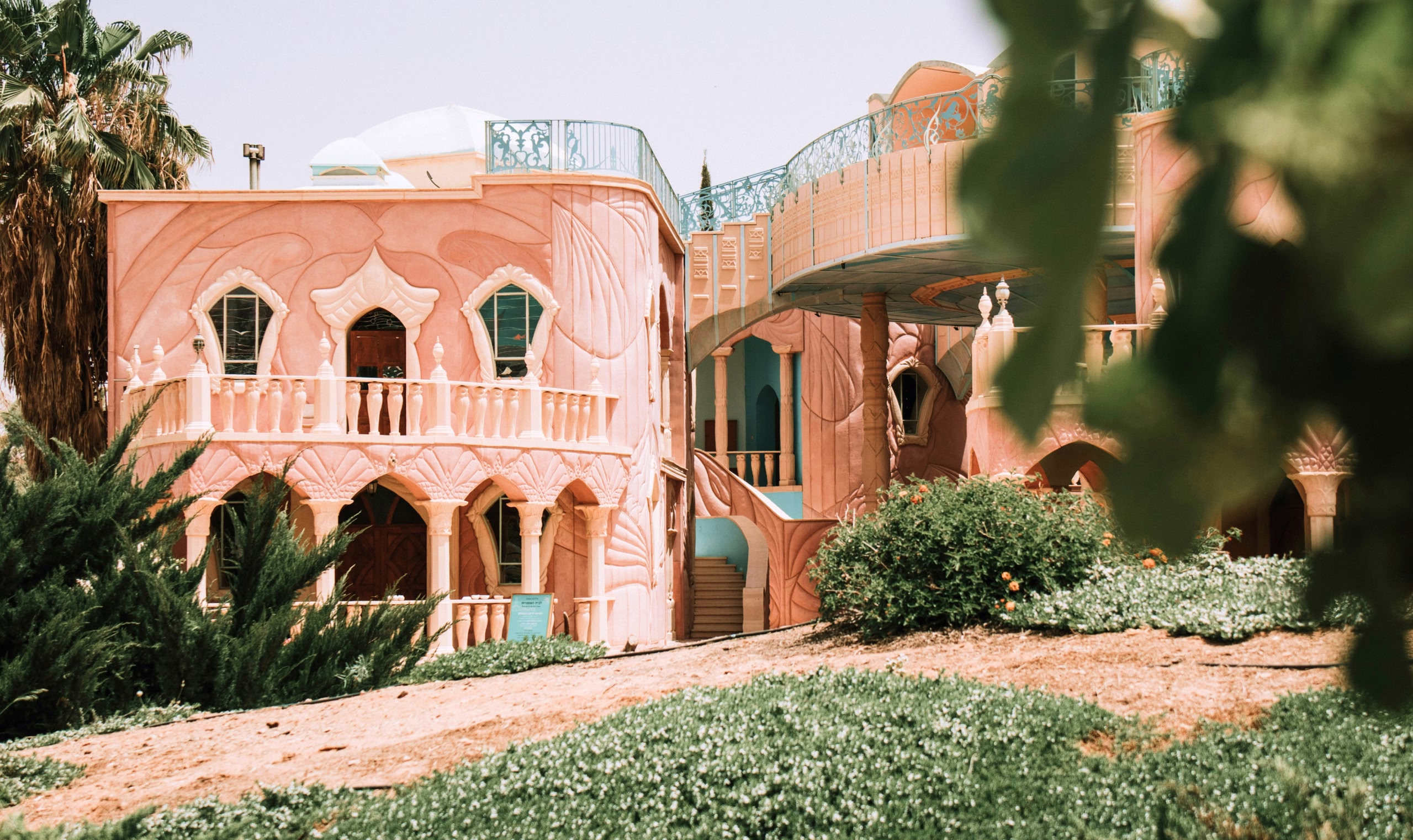 Elaborate, pink house with curved sides and balustrade, overlooked by a garden