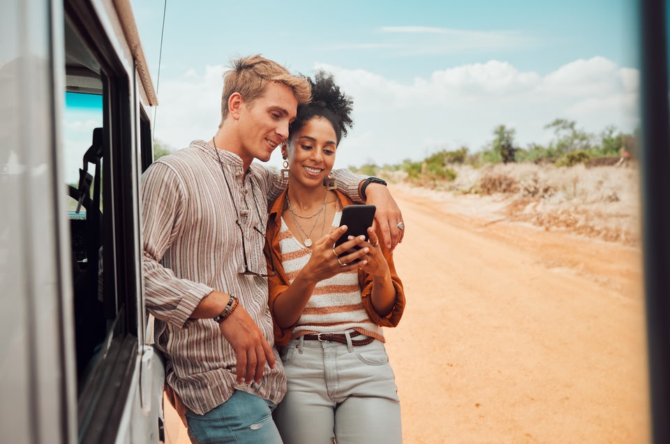 Una pareja parada afuera de su auto y mirando juntos su teléfono.