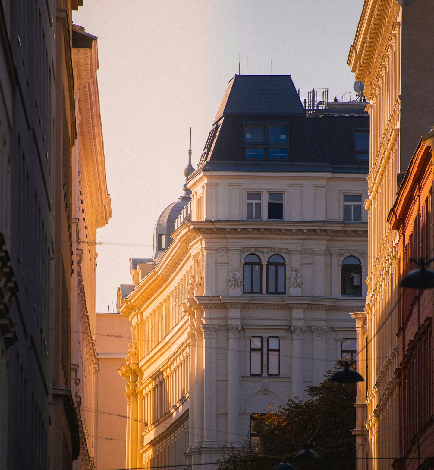 An majestic old white building with a grey slate roof is lit by the sun on a street in Vienna, Austria