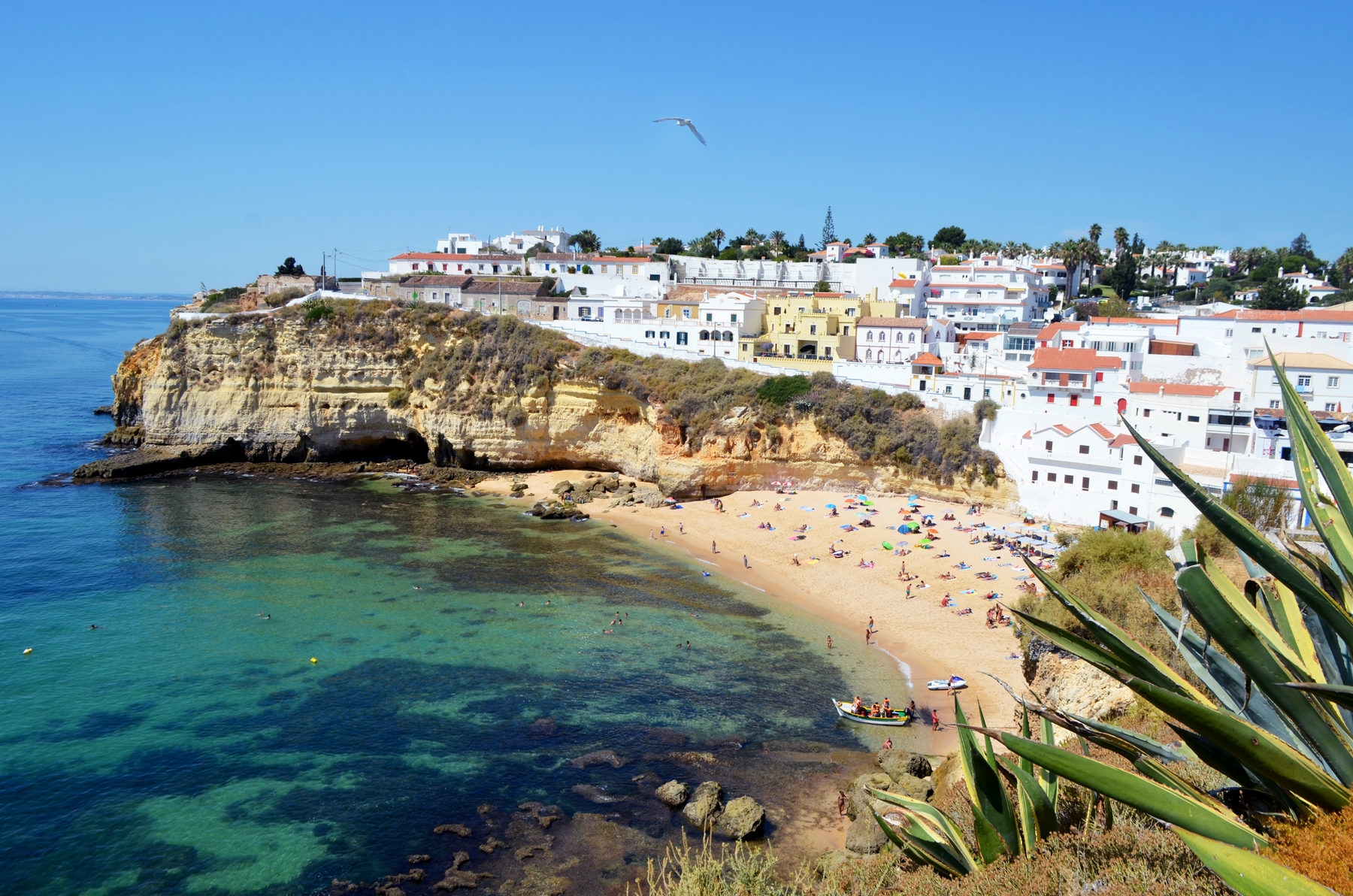 People basking on a sandy beach in the Algarve, Portugal, with whitewashed buildings perched on a clifftop