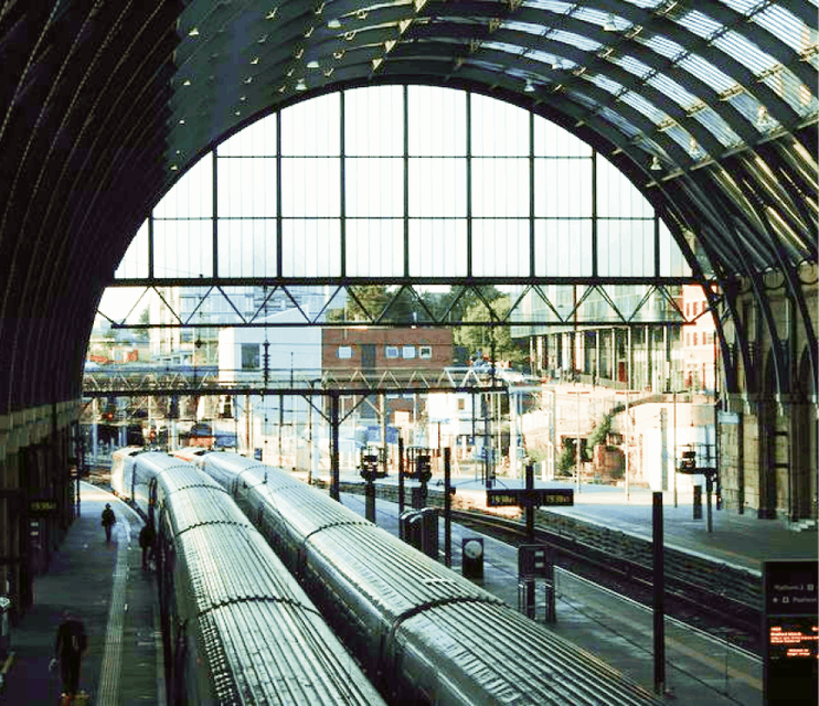 Aerial view of two parallel train carriages stationed at London King's Cross station. Bathed in sunlight on a bright summer day, the cityscape in the distance adds a picturesque backdrop, creating a scene of urban tranquility and travel anticipation.