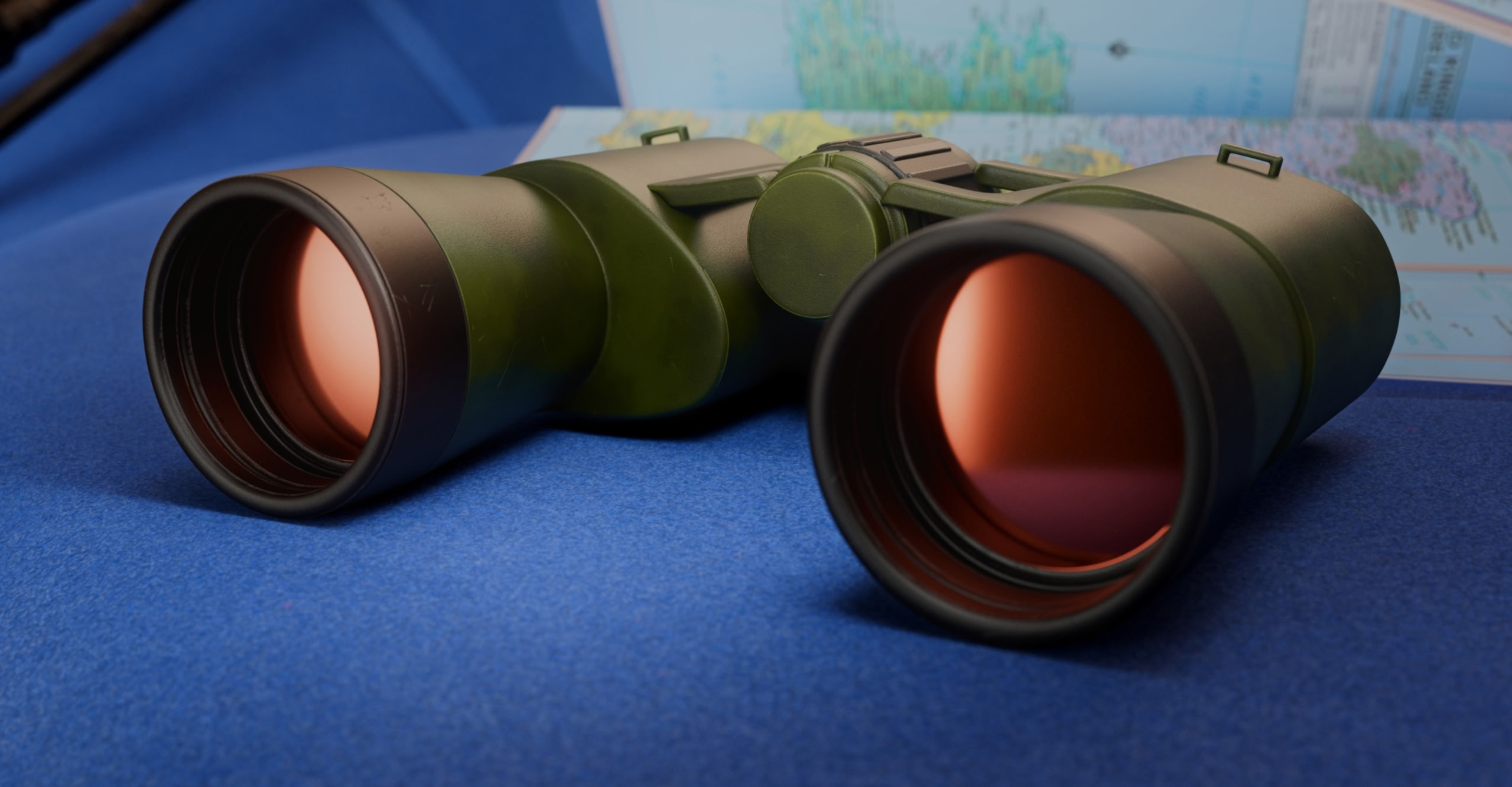 A close up of a pair of green binoculars with red lenses sitting on blue fabric with a map in the background