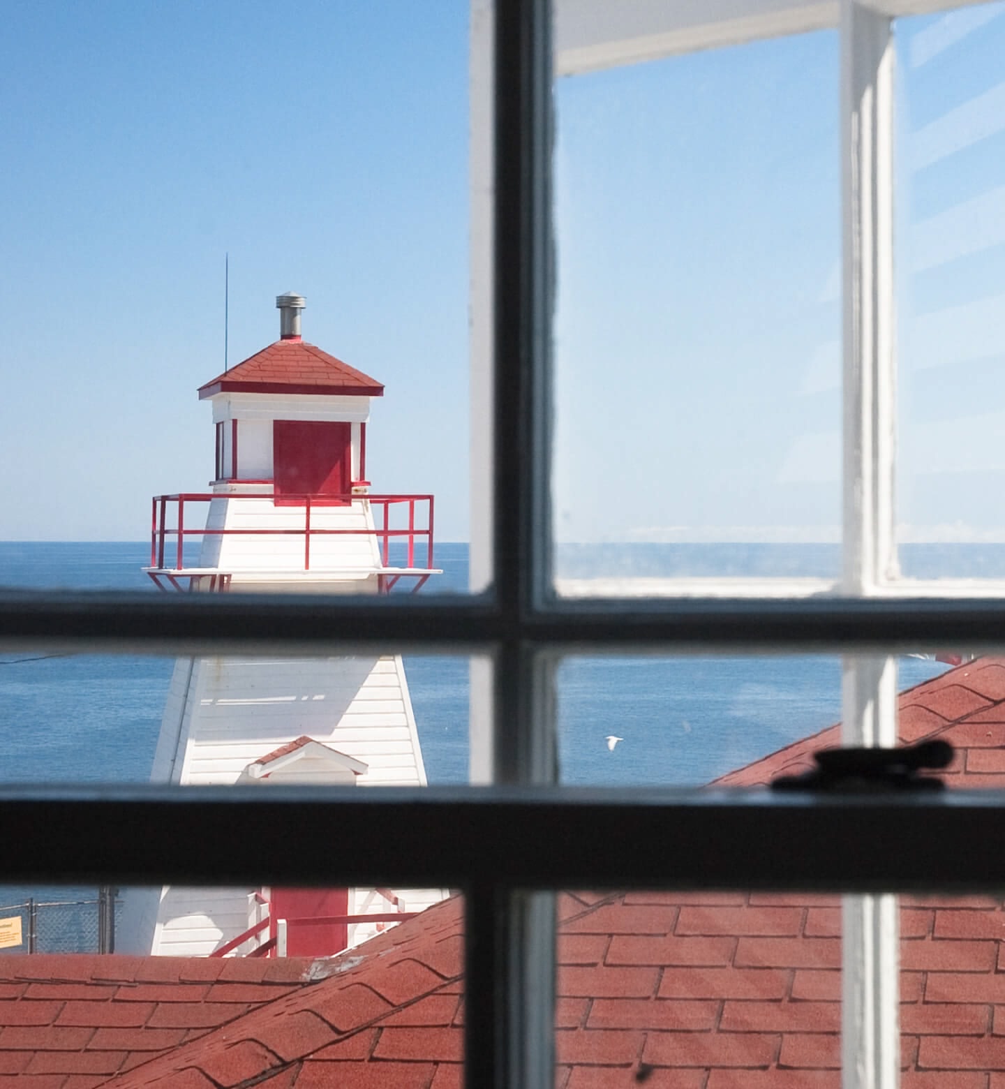 A white and red lighthouse set in front of the sea seen through a window in St Johns, Canada