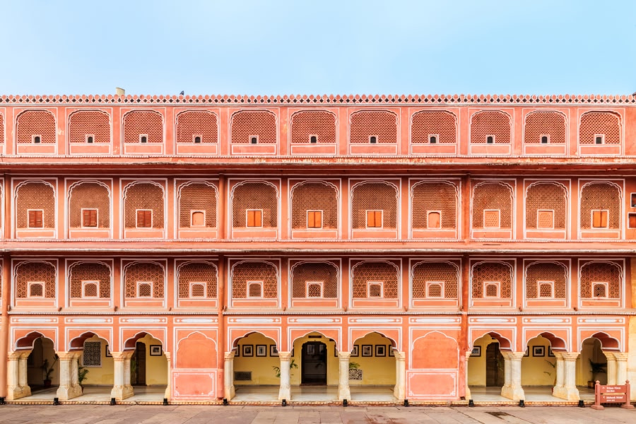 The grand pink-painted facade of the City Palace in Jaipur, displaying multiple stories of arched windows, decorative balconies, and carved ornamentation in the iconic terracotta-pink hue of Jaipur's historic architecture.