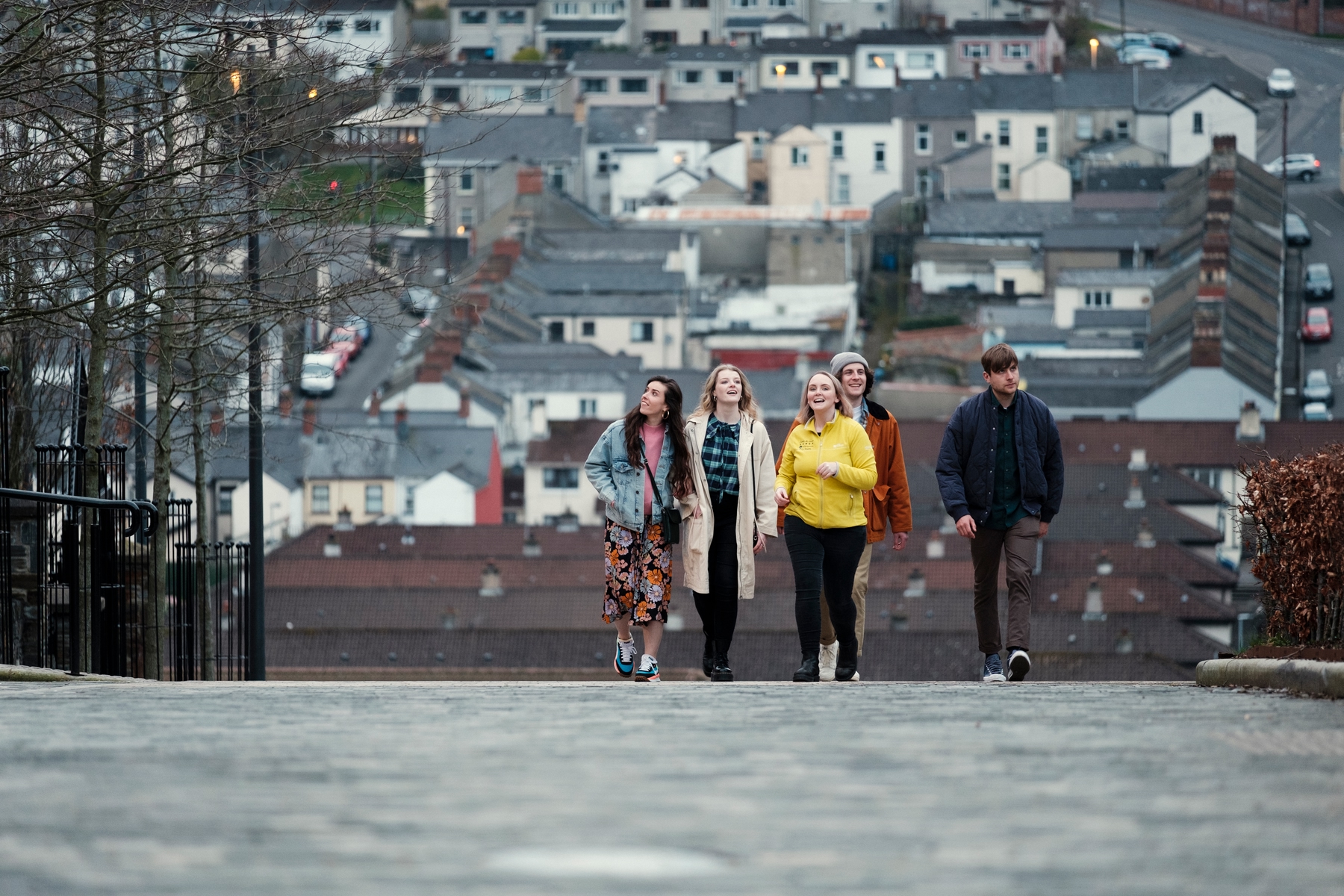 Group of three girls and two boys walking with houses in the background, on a Derry Girls tour of Derry/Londonderry.
