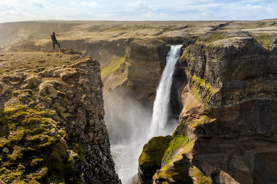 Traveller on top of a cliff watches a waterfall - best time to visit Iceland