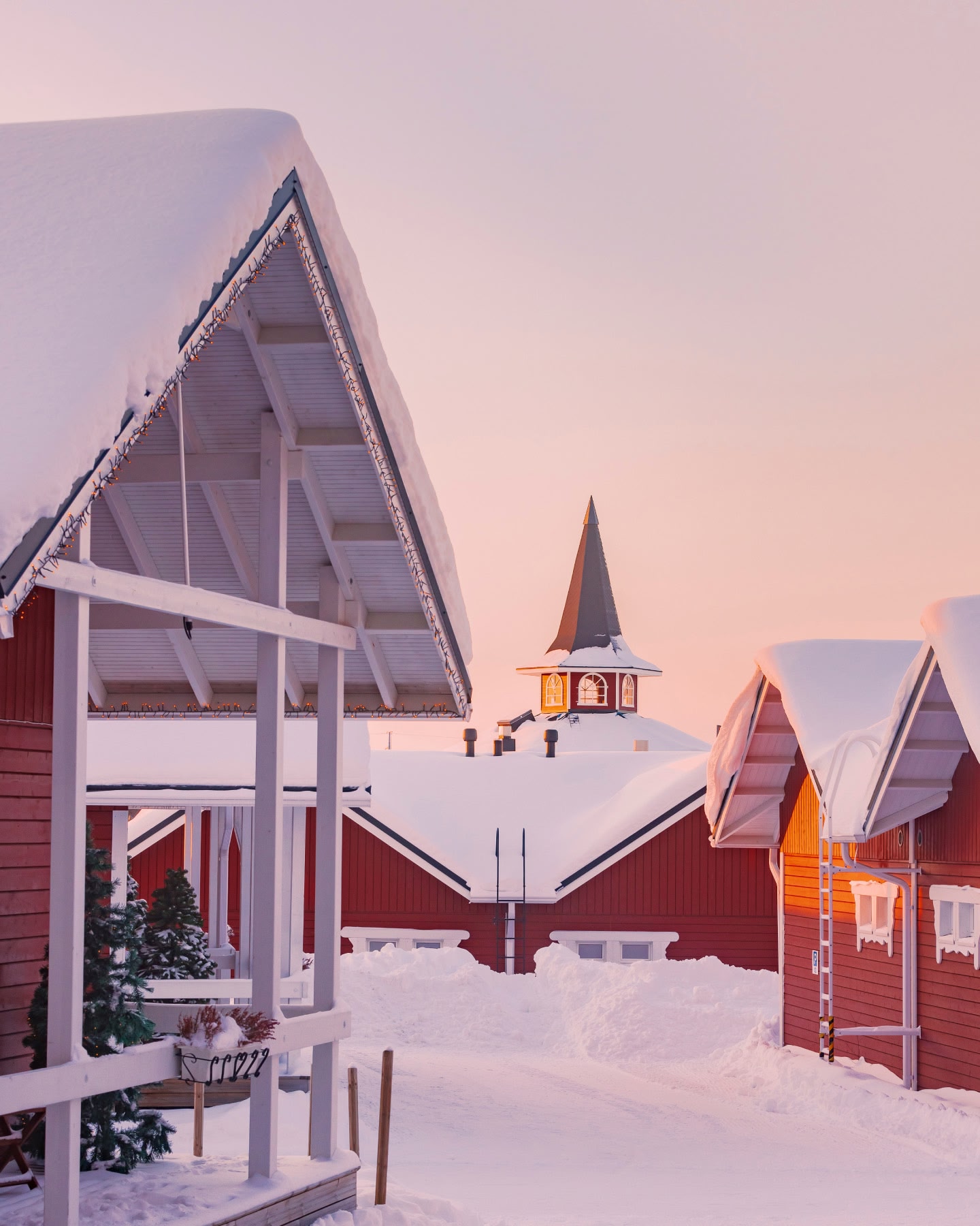 Rote, schneebedeckte Holzhäuser und ein schneebedeckter Kirchturm in der Abenddämmerung in Rovaniemi, Finnland.