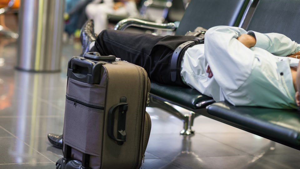 un homme s'est allongé sur des chaises d'aéroport avec sa valise à côté de lui
