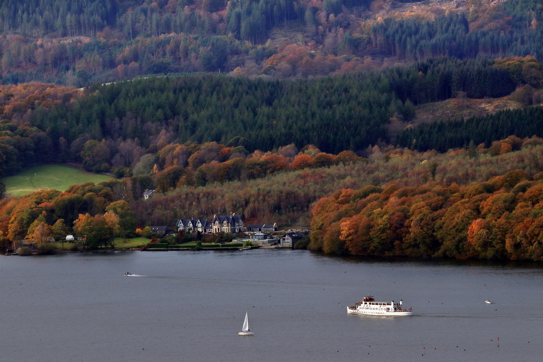 Boats sailing on Lake Windermere, with autumn leaves on the shore