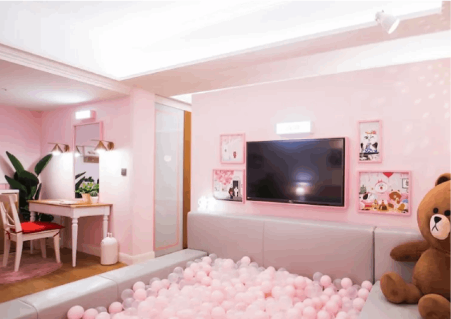 Inside a Splaisir Seoul Myeong-dong hotel room, a charming children's playroom unfolds in a soft pink hue, featuring a ball pit, a large teddy bear, and a tv for entertainment.