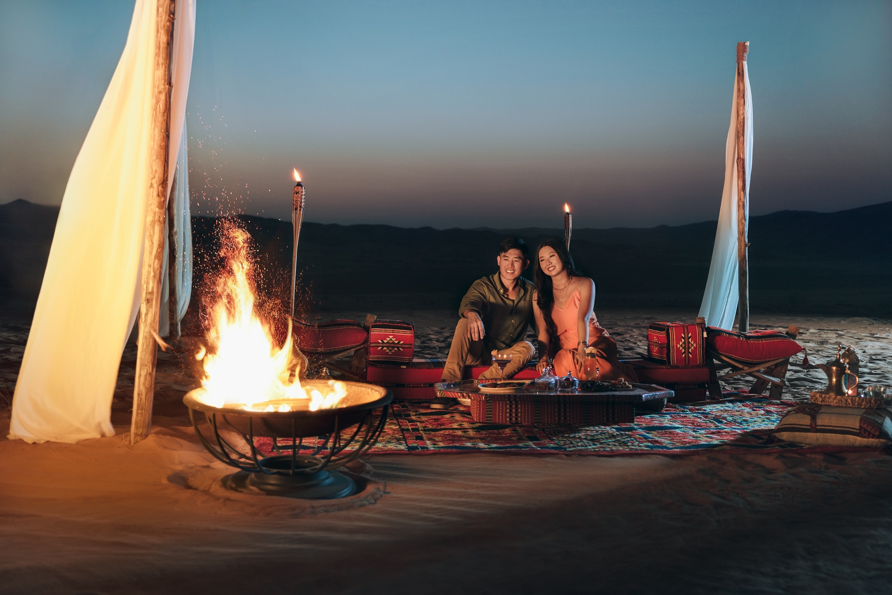 Couple assis dans le désert regardant un feu de camp.